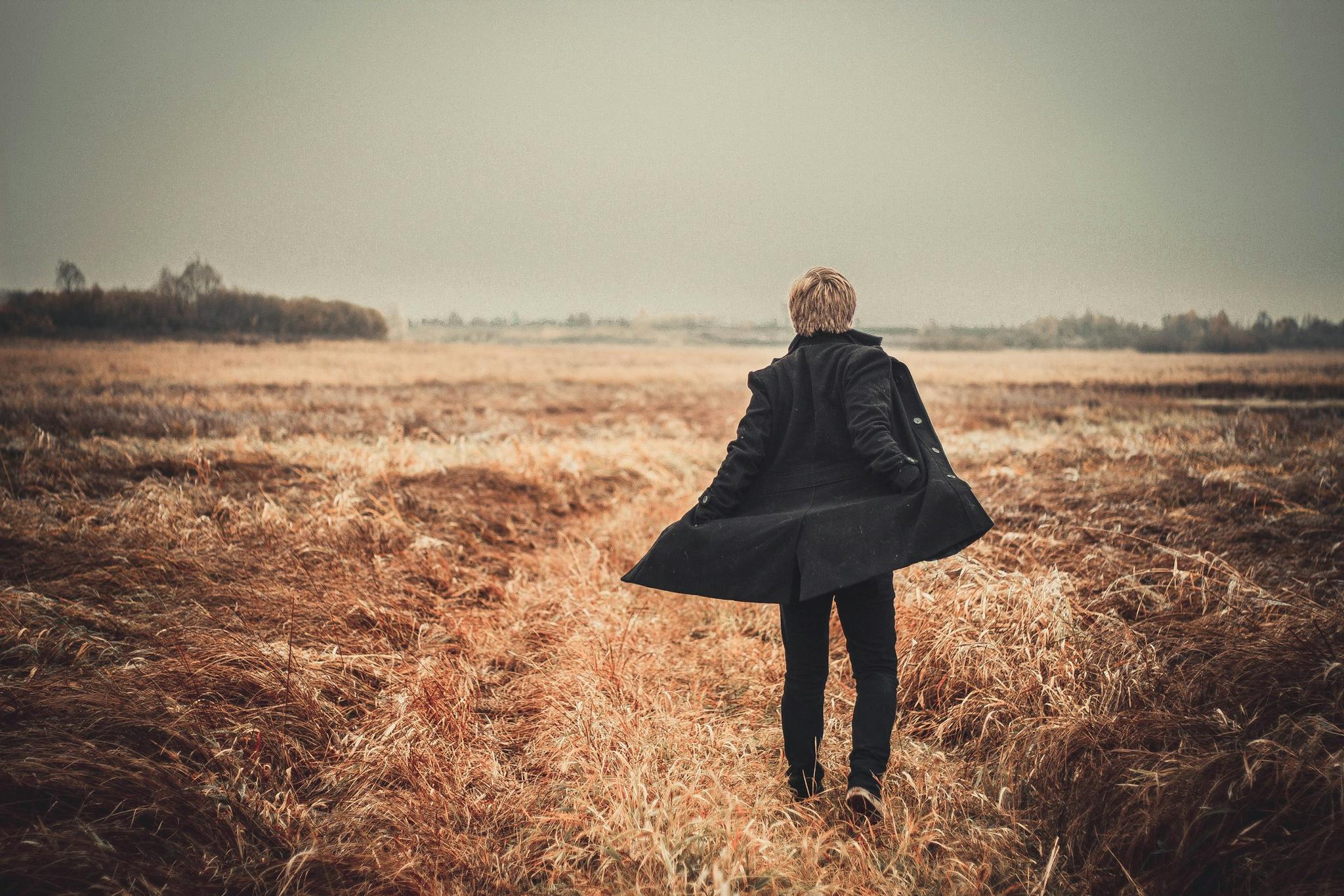 A person walks alone in a scenic autumn field wearing a coat.