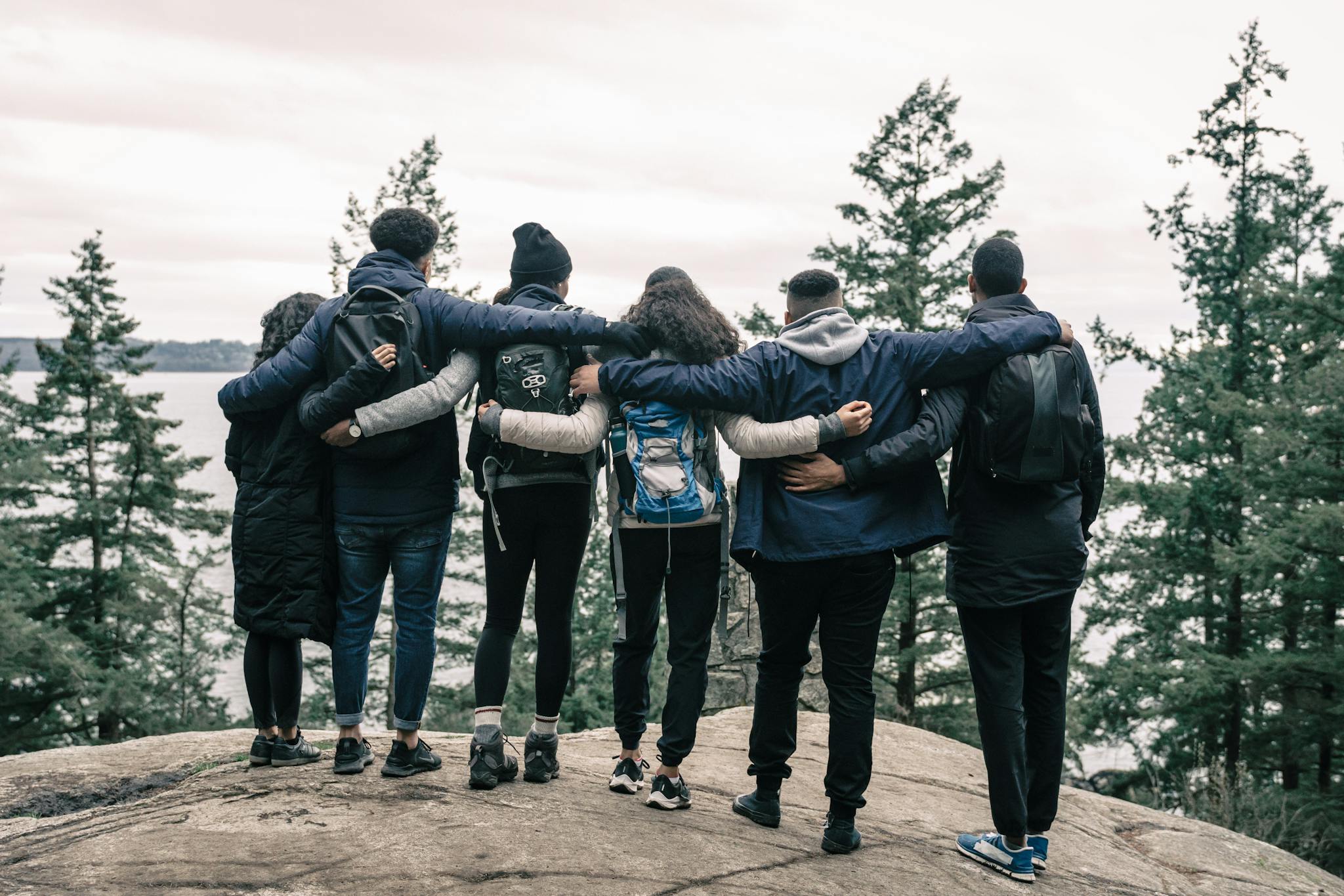 Back view of friends embracing on a scenic cliff, enjoying nature and friendship.