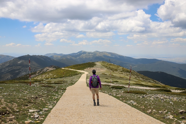 A hiker with a backpack walking through a road on a hill covered in greenery - concept of success CREATOR: gd-jpeg v1.0 (using IJG JPEG v80), quality = 100